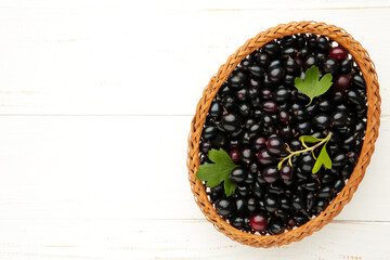 Basket with black currant on white wooden background