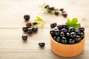 Black currant with leaf in wooden bowl on grey wooden table