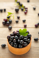 Black currant with leaf in wooden bowl on grey wooden table. Vertical foto