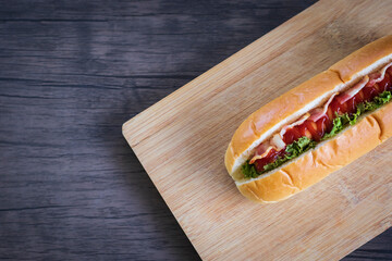Sausage sandwich with ham, cheese, bacon, lettuce, on a cutting board