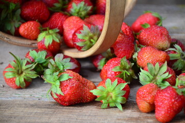 Ripe strawberries with leaves in wicker basket on wooden table on blurred background