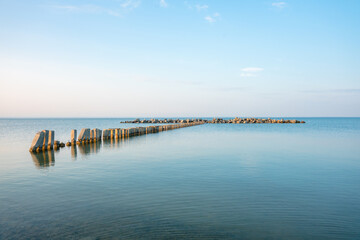 Calm morning sea surface with old stone pier and rocks. Morning seascape.
