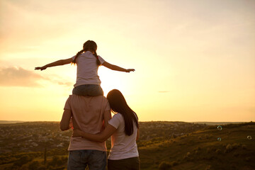 Fototapeta premium Back view of peaceful family watching sunset at mountains, copy space. Parents with child enjoying evening scenery