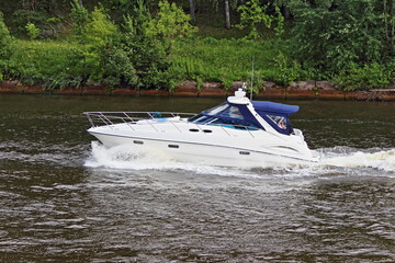 Modern white cabin awning plastic motor boat with inboard motor floats right to left on river water...