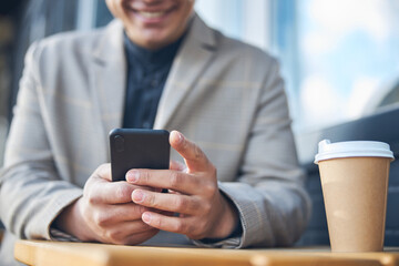 Smiling young man using modern smartphone in outdoor cafe