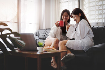 Cropped shot view beautiful young asian women LGBT lesbian happy couple sitting on sofa using laptop a computer and phone in living room at home. LGBT lesbian couple together.