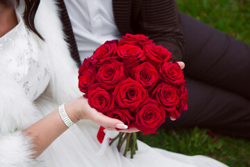 the groom in a suit and the bride in a white wedding dress hold a bouquet of red roses. Image with selective focus