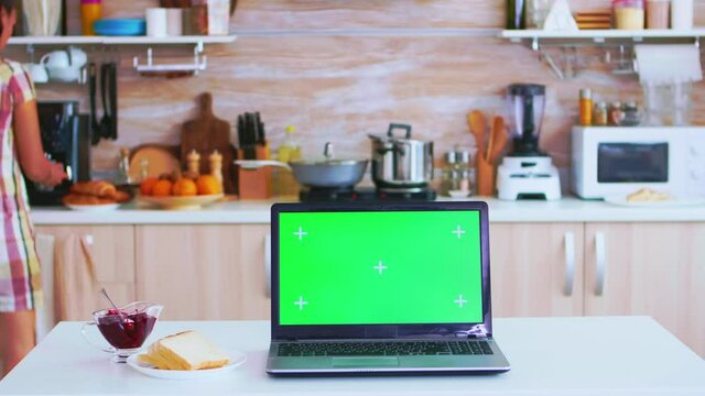 Laptop with green copy space available in kitchen and woman preparing for breakfast. Delicious french pastry. Green screen chroma mock up isolated mockup background ready to be replaced with your text