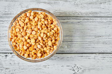 Raw yellow dry peas in a transparent glass plate on wooden background. Closeup, top view