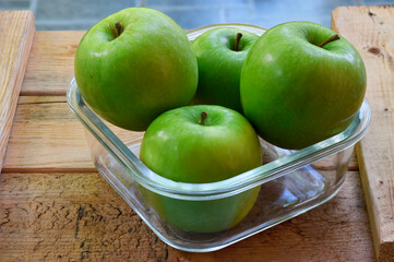 Four green apples in a glass bowl