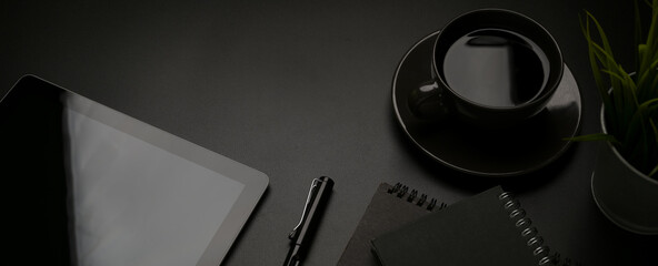 Dark office desk with digital tablet, stationery, pen, coffee cup and copy space