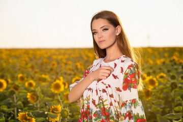 Naklejka na ściany i meble Beautiful young girl posing at sunset in a sunflower field