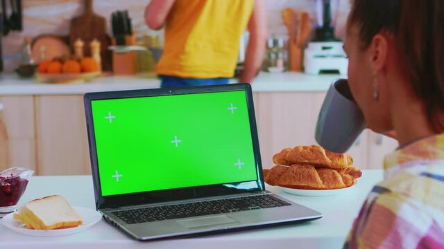 Freelancer using laptop with copy space available in kitchen and boyfriend is cooking morning meal. Green screen chroma mock up isolated mockup background ready to be replaced with your text, logo or