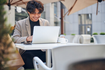 Cheerful young man using laptop in outdoor cafe