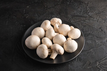 Champignon mushrooms healthy food on black plate on dark black textured background, angle view copy space