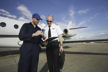 Plane engineer and pilot looking at document on clipboard