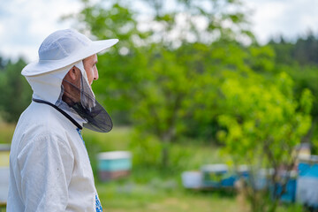 Beekeeper in protective workwear. Hives background at apiary. Works on the apiaries in the spring.
