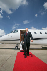 Businessman walking on red carpet upon exiting private jet