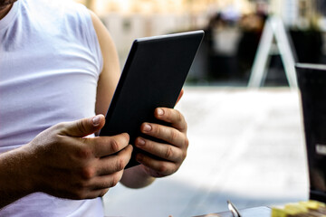Man using a tablet computer while relaxing in a coffee shop.Unrecognized person using tablet for conversation while relaxing on sofa in modern cafe.Concept of young man working out side of office.