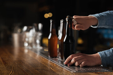 Fototapeta na wymiar Evening with company in pub. Barman opens beer bottles on wooden bar counter