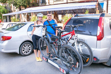 Man and woman are standing near two bicycles mounted on trunk of car.