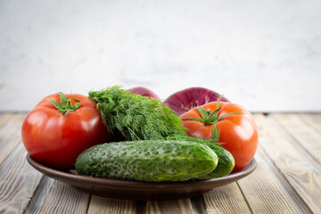 On a plate are vegetables, tomatoes, cucumbers, onions and dill. Fresh vegetables close-up. Natural food.