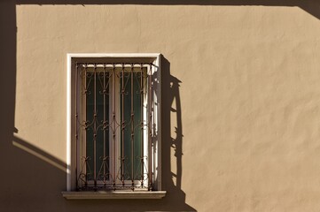 An isolated white window with rusted gratings in an ocher wall (Pesaro, Italy, Europe)