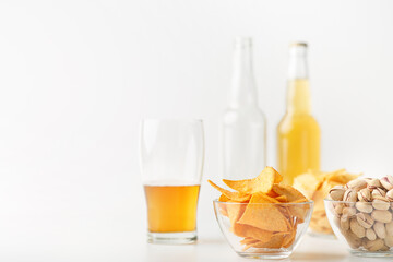 Set of snacks and beer for clients. Half glass of beer, empty and full bottle, nachos, chips and pistachios in glass plates