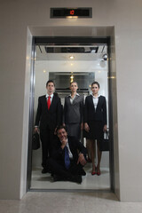 Business people standing while businessman sitting on the floor of elevator
