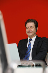 Businessman talking on telephone headset while using laptop