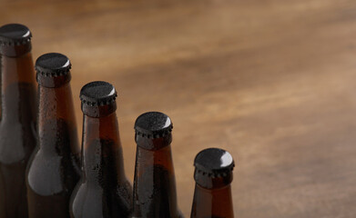 Beer industry. Row of dark beer bottles with caps on wooden background