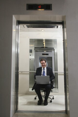 Businessman sitting on office chair and using laptop in elevator