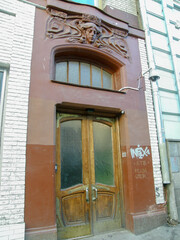 An ancient entrance to the house with a double wooden door with glass and a woman's head surrounded by a floral ornament above it