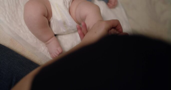Physiotherapist massages little newborn baby's foot and fingers on home bed