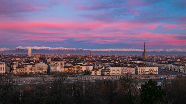 Time lapse: sunrise at Torino Italia (Turin, Italy). The skyline and the Mole Antonelliana tower over the buildings. Colorful dramatic sky and mountain range (the Alps) in background