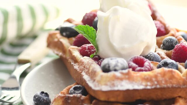 Belgian waffles on plate with ice cream and berries. Sweet waffle breakfast. Dessert served on table with napkin and fork.
