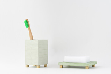 Eco natural wooden bamboo toothbrush in a holder and a soap in a soap dish. Minimal bathroom design, isolated. Natural light.