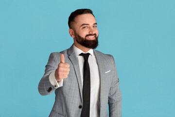 Cheerful millennial businessman showing thumb up gesture on blue background