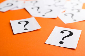 Paper notes with question marks on orange background, closeup