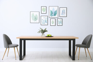 Fototapeta na wymiar Stylish room interior with modern table, chairs and paintings of tropical leaves. Idea for design