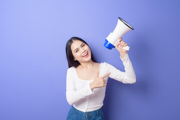portrait of young beautiful smiling woman is using megaphone to announce over isolated purple background studio
