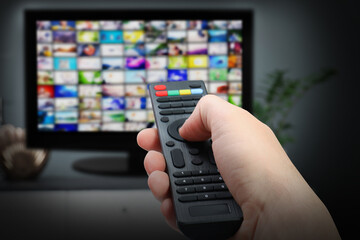 Streaming video services. Woman using remote control to change channels on TV, closeup