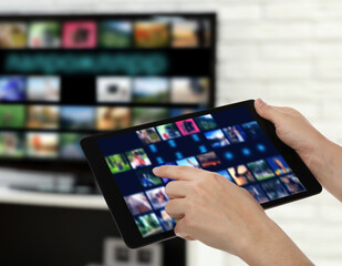 Streaming video services. Woman using tablet to change channels on TV, closeup