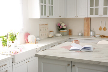 Book and cup on white marble table in modern kitchen. Interior design