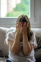 A sad woman raise hand off her face, while sitting in front of her bed. Sad young woman sitting alone in a empty room. Domestic violence, international women's day.