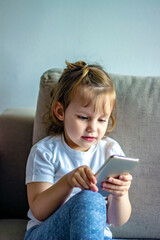 Cute girl chatting on the internet with smartphone social media app sitting in bed at home. Technology education and children mobile abuse. Little girl watching cartoons on a gold smartphone.