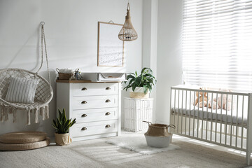 Chest of drawers with changing tray and pad near comfortable cradle in baby room. Interior design