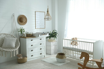 Chest of drawers with changing tray and pad near comfortable cradle in baby room. Interior design