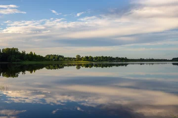 Foto op Canvas Prachtig landelijk landschap met een meer. Wolken worden weerspiegeld in het water. Dorp in de buurt van het meer. Zomer op het platteland. © Andrei Stepanov