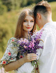 Beautiful young couple in love on a blooming field with a bouquet of bright lupine flowers